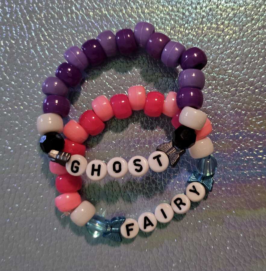 Two simple kandi singles that say 'FAIRY' and 'GHOST'. The 'FAIRY' single has light pink and hot pink beads, while 'GHOST' has light purple and dark purple..